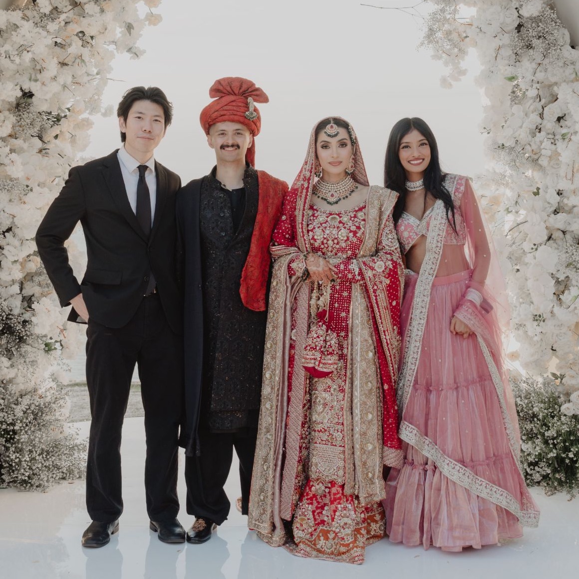 The four Almari co-founders together at a wedding, under an arch of white flowers.